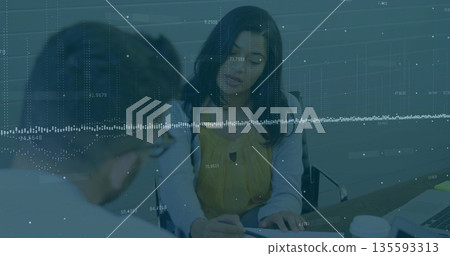 Woman in yellow blouse examining paperwork on desk in office meeting area, with laptop, coffee cups 135593313