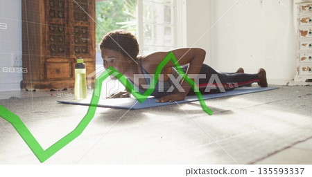 Woman in sportswear performing back extension on yoga mat in living room, water bottle overlay 135593337