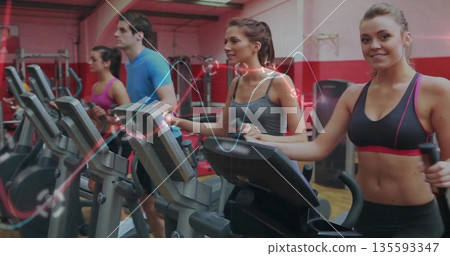 Woman in sportswear pedaling on rightmost elliptical in cardio area, with weight racks, copy space Woman in sportswear pedaling on rightmost elliptical in cardio area, with weight racks, copy space 135593347