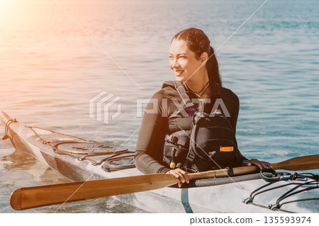Kayaking Woman Sea Smiling woman in wetsuit paddling kayak on calm sea. Kayaking Woman Sea Smiling woman in wetsuit paddling kayak on calm sea. 135593974