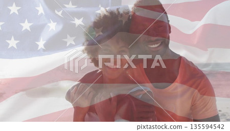 Hugging couple standing on sandy shoreline, under translucent American flag overlay Hugging couple standing on sandy shoreline, under translucent American flag overlay 135594542