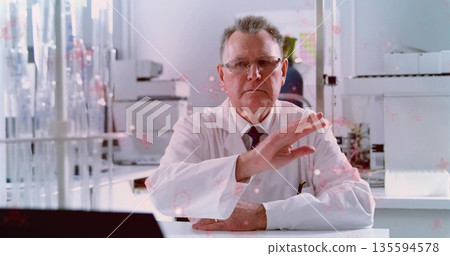 Sitting senior scientist wearing lab coat analyzing samples at lab bench, with test tube racks 135594578