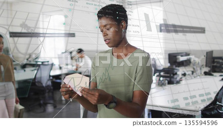 Designer inspecting pink geometric prototype at desk in open plan office, with monitors Designer inspecting pink geometric prototype at desk in open plan office, with monitors 135594596