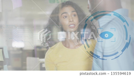 Woman wearing yellow top discussing data behind glass with circuit overlay and eye HUD in office Woman wearing yellow top discussing data behind glass with circuit overlay and eye HUD in office 135594619