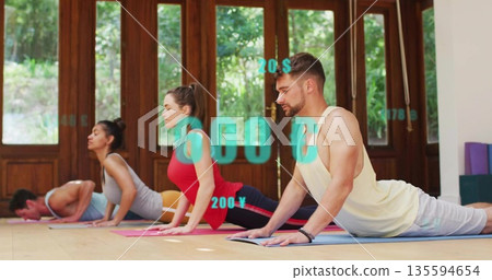 Four adults performing upward-facing dog pose in yoga studio, colorful mats and foam blocks 135594654