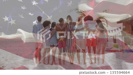 Leaning friends placing arms around shoulders on sandy shoreline, with hut bunting flags cushions 135594664