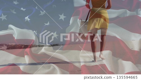 Striding woman in yellow sundress holding tote bag on beach with US flag overlay, copy space Striding woman in yellow sundress holding tote bag on beach with US flag overlay, copy space 135594665