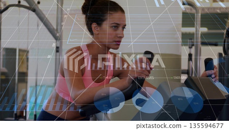 Training woman wearing pink sports bra with leggings on elliptical in gym with data chart overlays Training woman wearing pink sports bra with leggings on elliptical in gym with data chart overlays 135594677