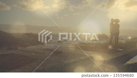 Embracing couple kissing on rocky shoreline at sunset, ocean waves and lens flares, copy space Embracing couple kissing on rocky shoreline at sunset, ocean waves and lens flares, copy space 135594680