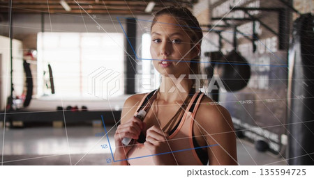 Standing woman wearing peach top in gym, with jump rope and punching bags showing numeric-overlay 135594725