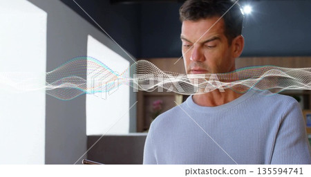 Man in blue sweater holding smartphone viewing waveform in office, with shelving, plant and books Man in blue sweater holding smartphone viewing waveform in office, with shelving, plant and books 135594741