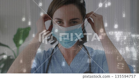 Clinician adjusting surgical mask in clinic, wearing blue scrubs, stethoscope, binary code overlay 135594757