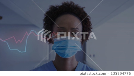 Standing woman wearing blue scrubs, surgical mask in hospital corridor, showing line chart overlay Standing woman wearing blue scrubs, surgical mask in hospital corridor, showing line chart overlay 135594776