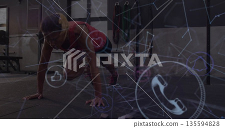 Mid-adult female wearing sportswear performing mountain climber exercise in gym, with digital icons Mid-adult female wearing sportswear performing mountain climber exercise in gym, with digital icons 135594828