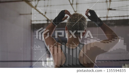 Raising arms female athlete standing in warehouse gym, with digital charts and fitness gloves Raising arms female athlete standing in warehouse gym, with digital charts and fitness gloves 135594835