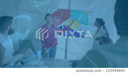 Pointing presenter wearing magenta blouse leading meeting in room at conference table, with monitor Pointing presenter wearing magenta blouse leading meeting in room at conference table, with monitor 135594845