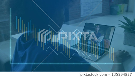 Listening woman wearing headphones reviewing charts on laptop at desk in office, with documents 135594857