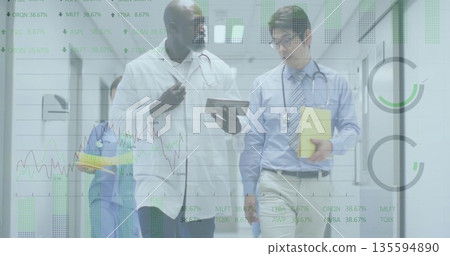 Two doctors walking and reviewing patient records in hospital corridor with tablet and folder 135594890