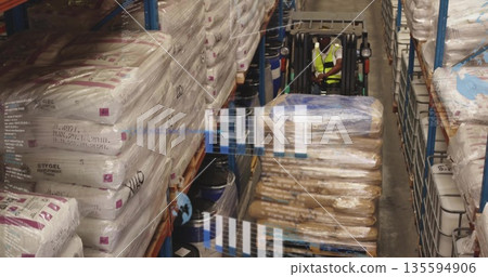 Forklift operator wearing reflective vest navigating pallet in warehouse aisle, with shelving racks 135594906