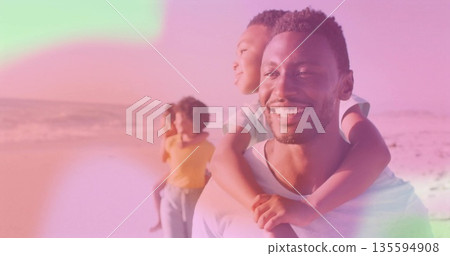 Father carrying son on shoulders walking along sandy beach during sunset, with pink sky, copy space 135594908