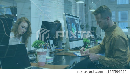 Man in tan shirt taking notes at monitor in office, with green pen, charts, copy space Man in tan shirt taking notes at monitor in office, with green pen, charts, copy space 135594911