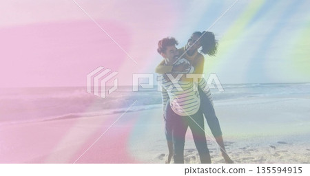 Laughing couple sharing piggyback ride on sandy shoreline, with mustard sweater and sunglasses 135594915