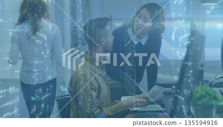 Seated man in mustard shirt reviewing documents in office with monitors, data reflections 135594916