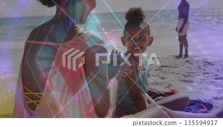 Mother and daughter playing on beach towels wearing swimsuits on shore, as father watching waves Mother and daughter playing on beach towels wearing swimsuits on shore, as father watching waves 135594917