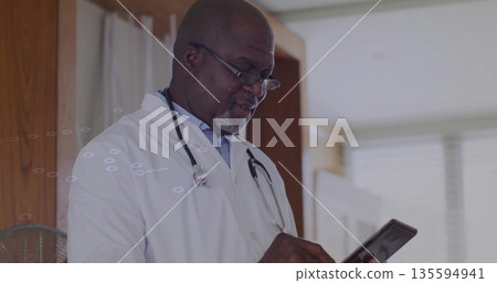 Reviewing data on tablet, senior doctor wearing lab coat, stethoscope and reading glasses in clinic 135594941