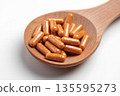 Golden curcumin capsules in a wooden spoon on a white table close up. Natural supplements 135595273