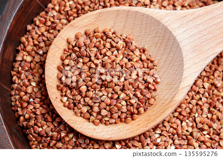 Raw buckwheat groats in a wooden spoon on a bowl filled with dry grains. Healthy cereal ingredient. Clean eating concept. Top view 135595276