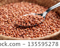 Metal spoon scooping uncooked buckwheat grains. Food storage concept 135595278