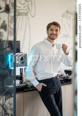 Smiling handsome man in white shirt having coffee in the office kitchen 135595605