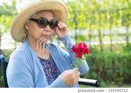 Asian senior woman holding red rose flower, smile and happy in the sunny garden. 135595712