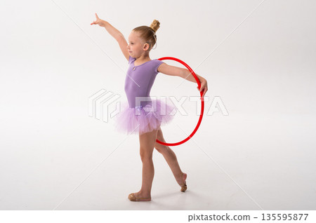 Little ballerina with cochlear implant performing pose with red hoop. Copy space. Inclusion, hearing awareness, and childhood empowerment through rhythm, color and balance. Copy space 135595877