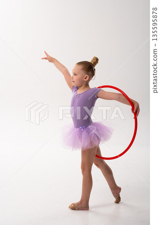 Young dancer with a cochlear implant balances with a red hoop during studio training. Inclusive performance, auditory support, and physical development through rhythmic gymnastics and ballet. Young dancer with a cochlear implant balances with a red hoop during studio training. Inclusive performance, auditory support, and physical development through rhythmic gymnastics and ballet. 135595878