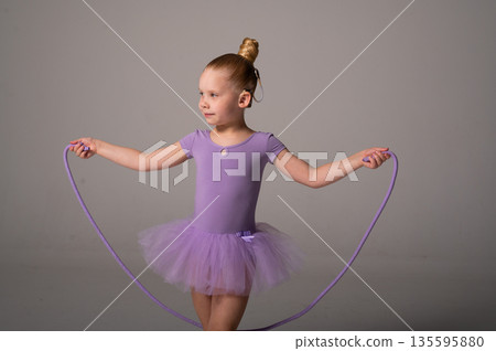Young dancer with a cochlear implant performs a rope exercise in a purple ballet costume. Inclusive sport, auditory technology, and physical coordination through rhythmic gymnastics and dance training 135595880