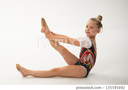 Side view of gymnast with cochlear implant stretching in studio leotard. Hearing rehabilitation, posture control and inclusive childhood physical development through rhythmic training 135595892