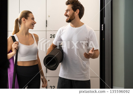 Cute blonde woman talking to a handsome bearded man in a gym changing room 135596092