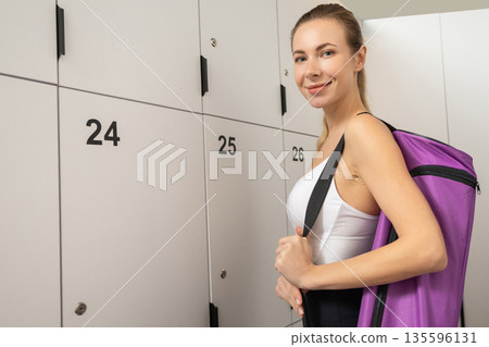 Cute blonde young woman with a violet bag opening locker in gym 135596131