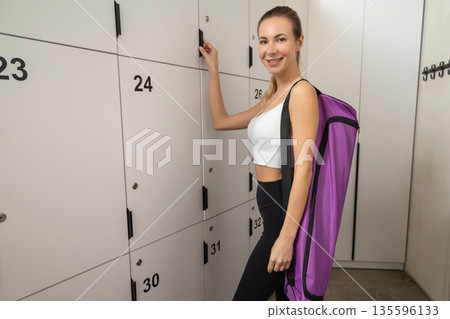 Cute blonde young woman with a violet bag opening locker in gym Cute blonde young woman with a violet bag opening locker in gym 135596133