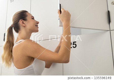 Long-haired blonde woman in a gym changing room opening the locker Long-haired blonde woman in a gym changing room opening the locker 135596149