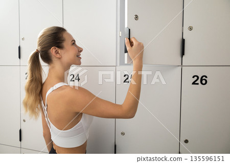 Long-haired blonde woman in a gym changing room opening the locker 135596151