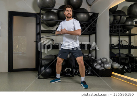 Dark-haired young sportsman exercising with elastic band and looking motivated 135596190