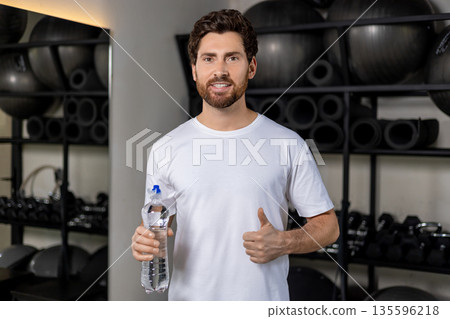 Dark-haired caucasian young man in the gym with a bottle of water in hands 135596218