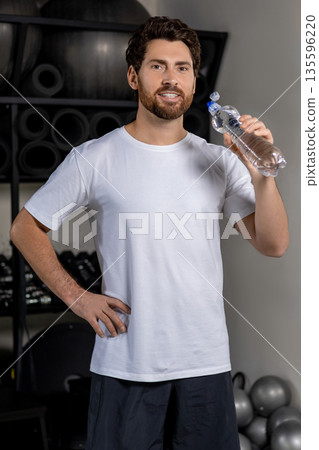 Dark-haired caucasian young man in the gym with a bottle of water in hands 135596220