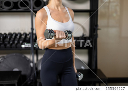 Long-haired blonde young woman exercising with dumbbells in the gym 135596227