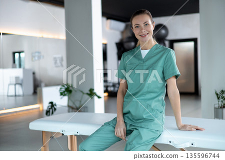 Woman physiotherapist sitting on couch smiling at camera preparing for session starting Woman physiotherapist sitting on couch smiling at camera preparing for session starting 135596744