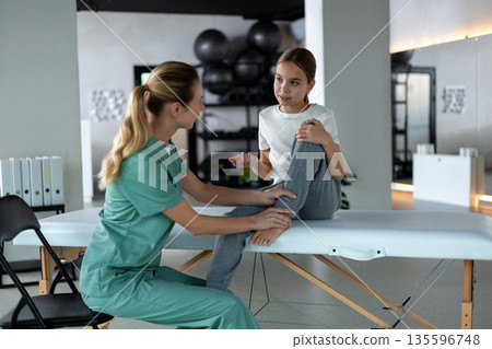 Physiotherapist helping young girl perform knee exercise Physiotherapist helping young girl perform knee exercise 135596748