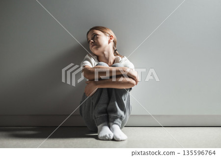 Child in defensive posture against gray background feeling deep emotional pain and solitude 135596764